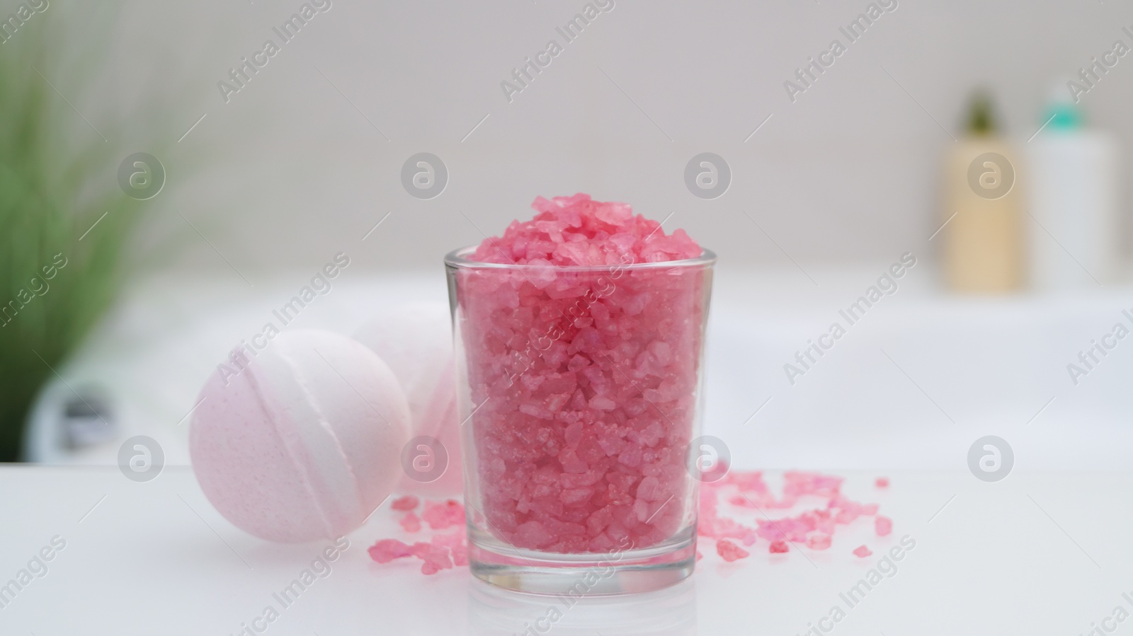 Glass with sea salt and bath bombs on table in bathroom, closeup Photo of Glass with sea salt and bath bombs on table in bathroom, closeup