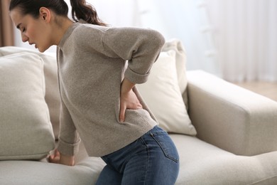Photo of Woman suffering from back pain at home. Bad posture problem