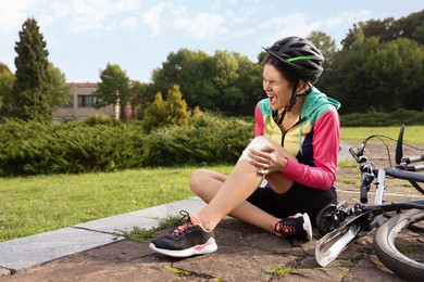 Photo of Young woman with injured knee near bicycle outdoors, space for text