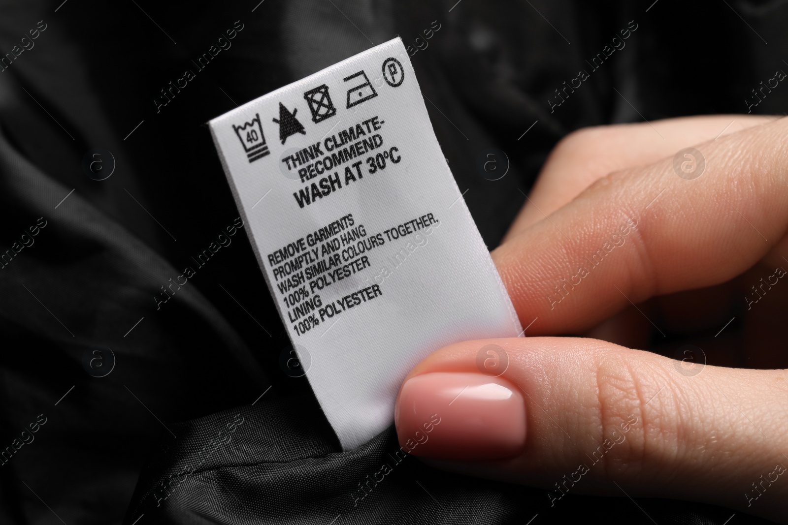 Photo of Woman holding clothing label on black garment, closeup