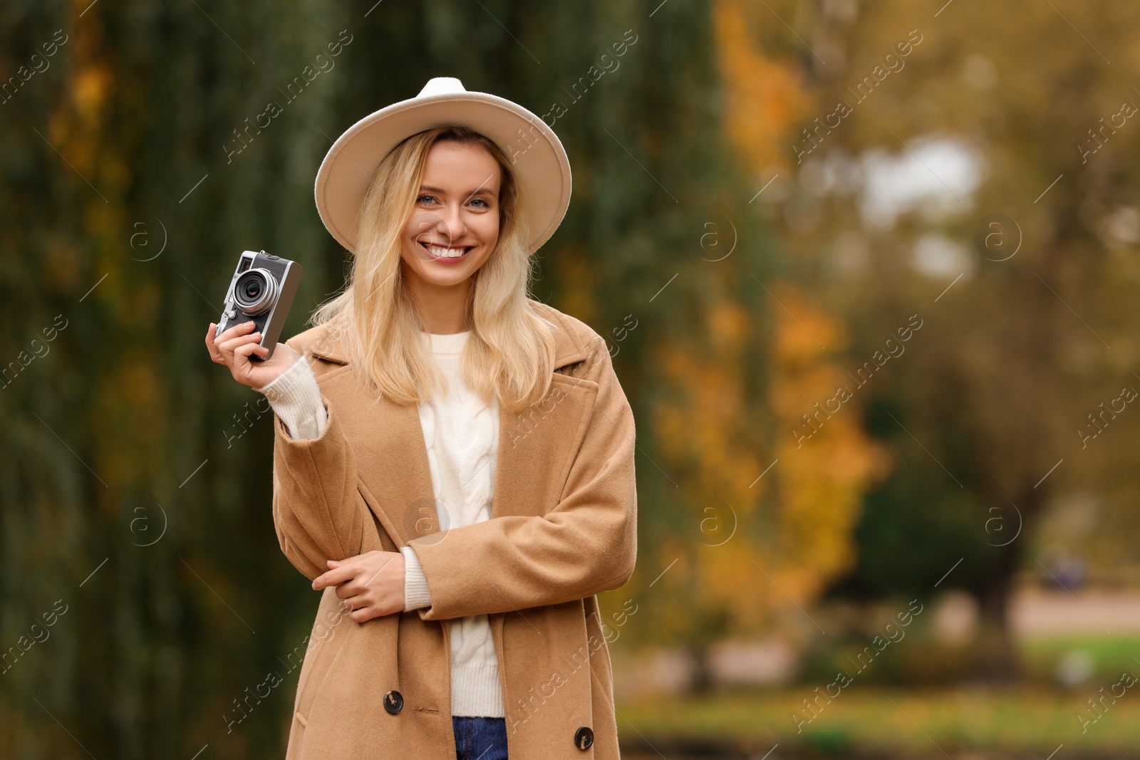 Photo of Portrait of happy woman with camera in autumn park. Space for text