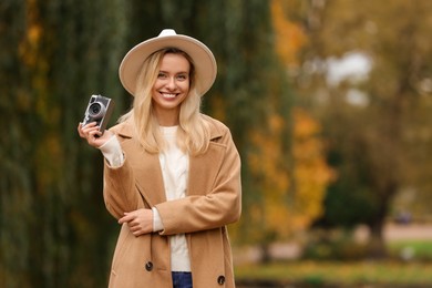 Portrait of happy woman with camera in autumn park. Space for text
