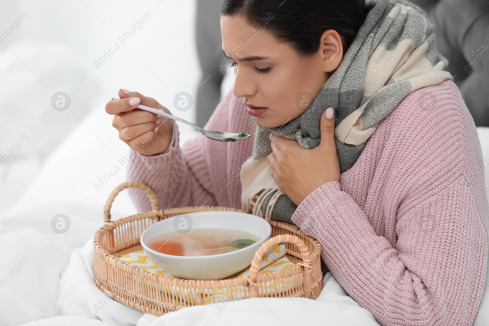 Photo of Sick young woman eating soup to cure flu in bed at home