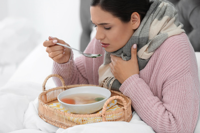 Photo of Sick young woman eating soup to cure flu in bed at home