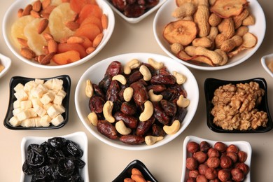 Photo of Bowls with dried fruits and nuts on beige background