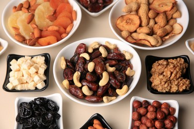 Bowls with dried fruits and nuts on beige background