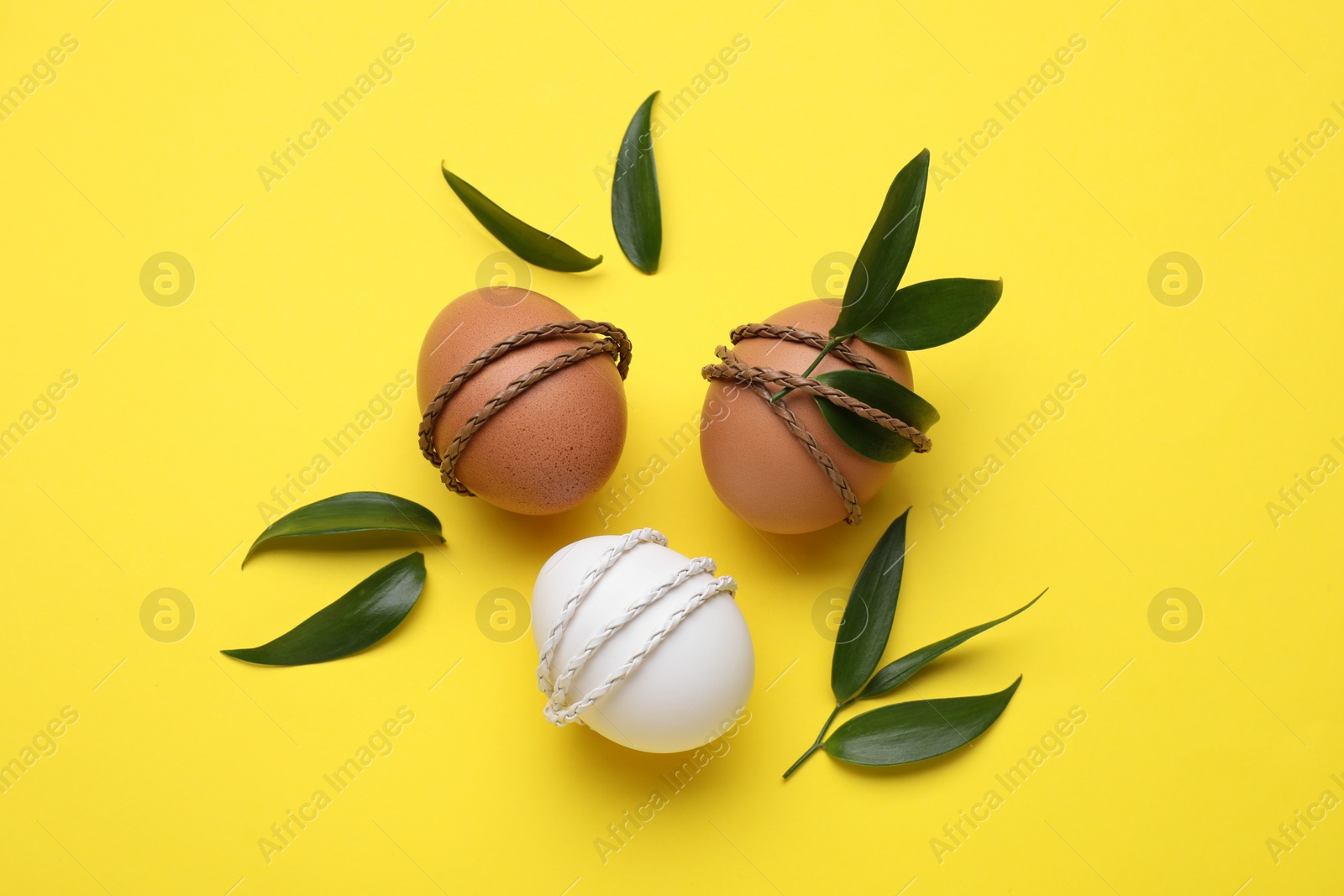 Photo of Easter eggs decorated with green leaves on yellow background, flat lay