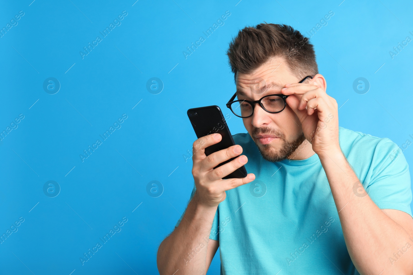 Photo of Man with vision problems using smartphone on blue background, space for text