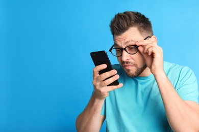 Photo of Man with vision problems using smartphone on blue background, space for text