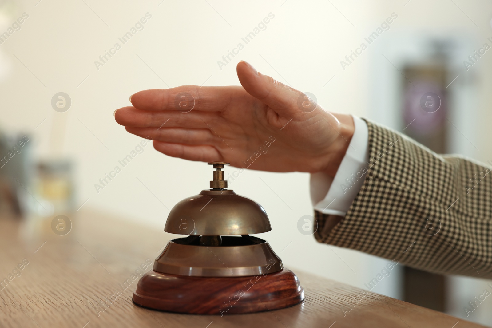 Photo of Woman ringing hotel service bell at wooden reception desk, closeup