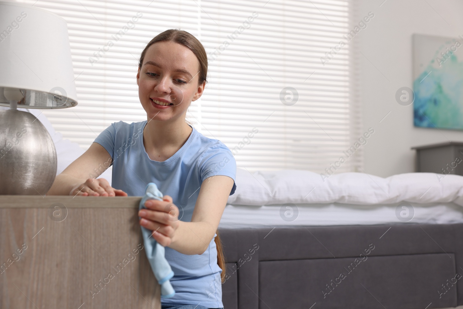 Photo of Woman with microfiber cloth cleaning wooden chest of drawers in room. Space for text