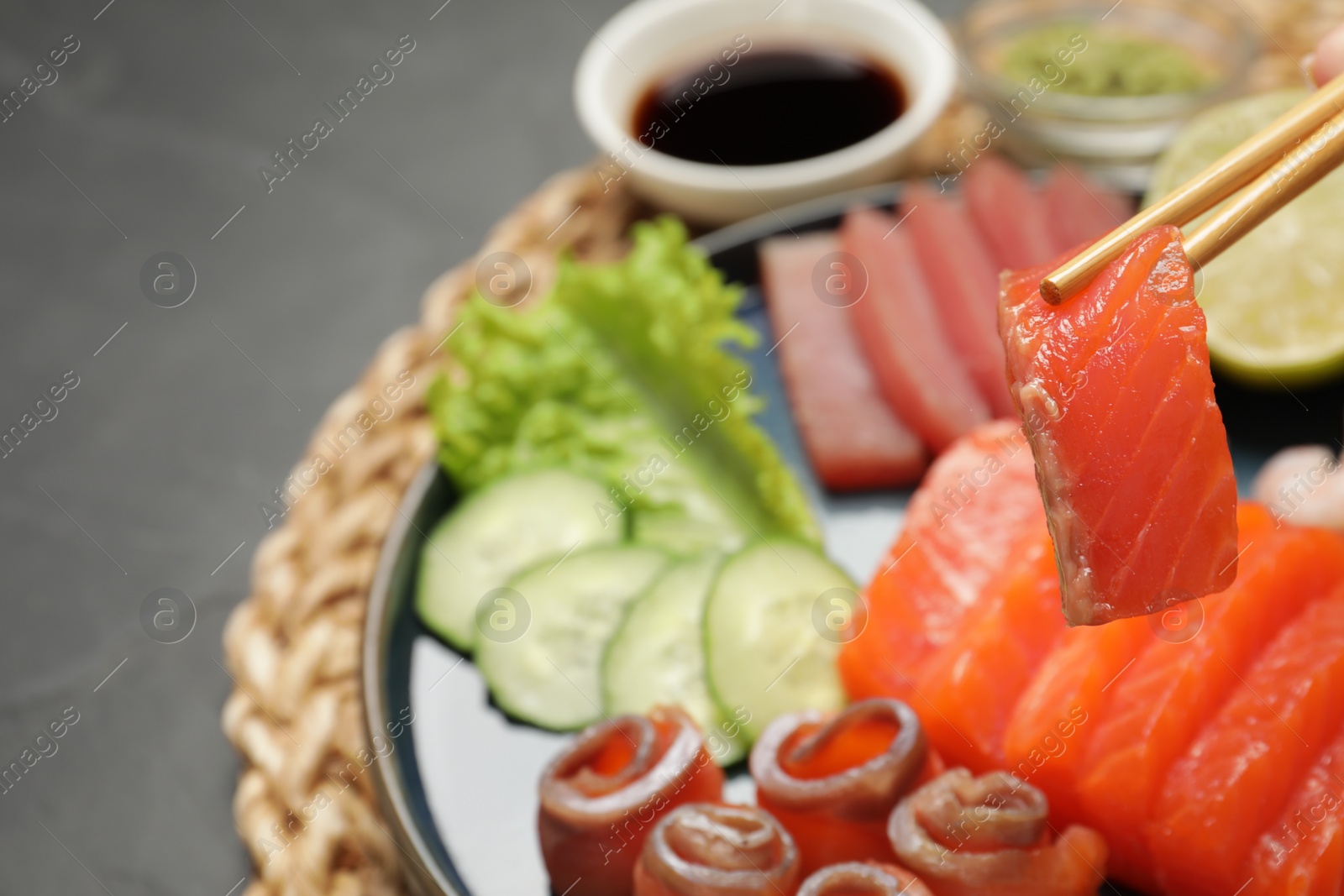 Photo of Taking tasty salmon slice with chopsticks at table, closeup. Delicious sashimi dish
