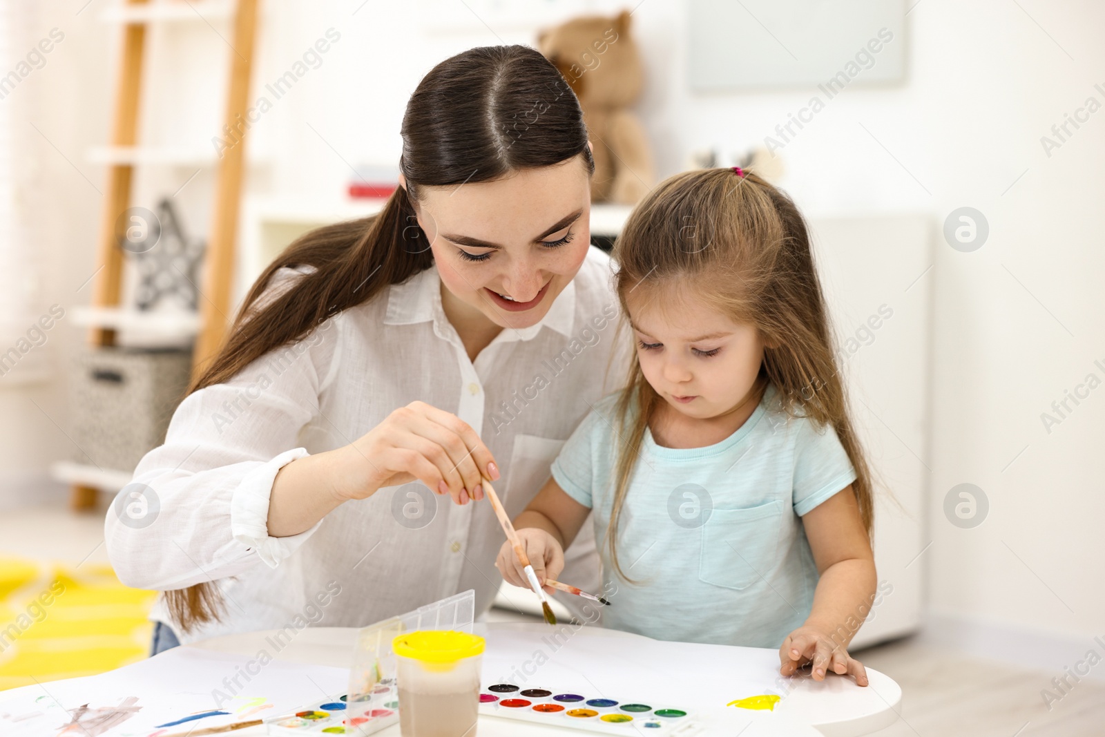 Photo of Mother and her little daughter painting with watercolor at home