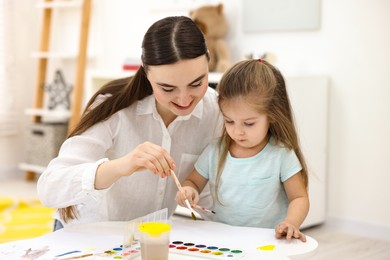 Mother and her little daughter painting with watercolor at home