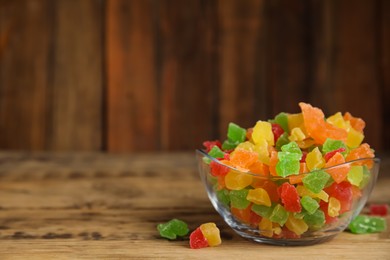 Photo of Mix of delicious candied fruits in bowl on wooden table. Space for text