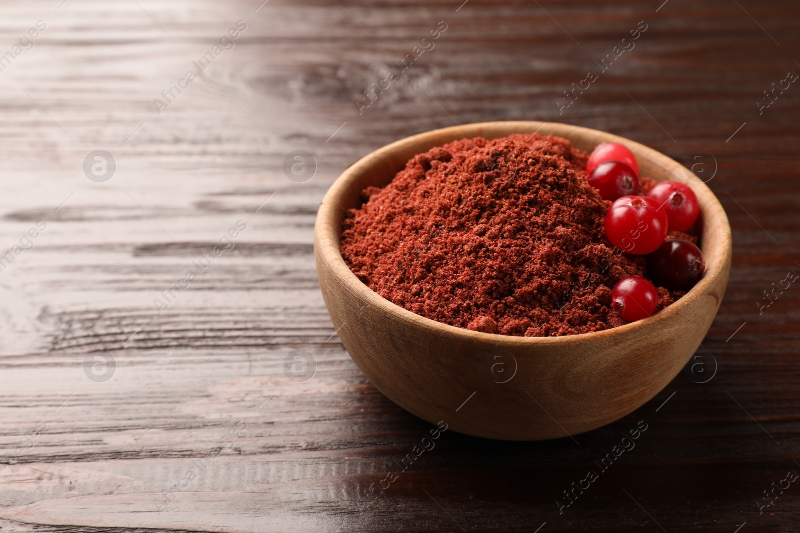 Photo of Dried cranberry powder and fresh berries in bowl on wooden table, closeup. Space for text