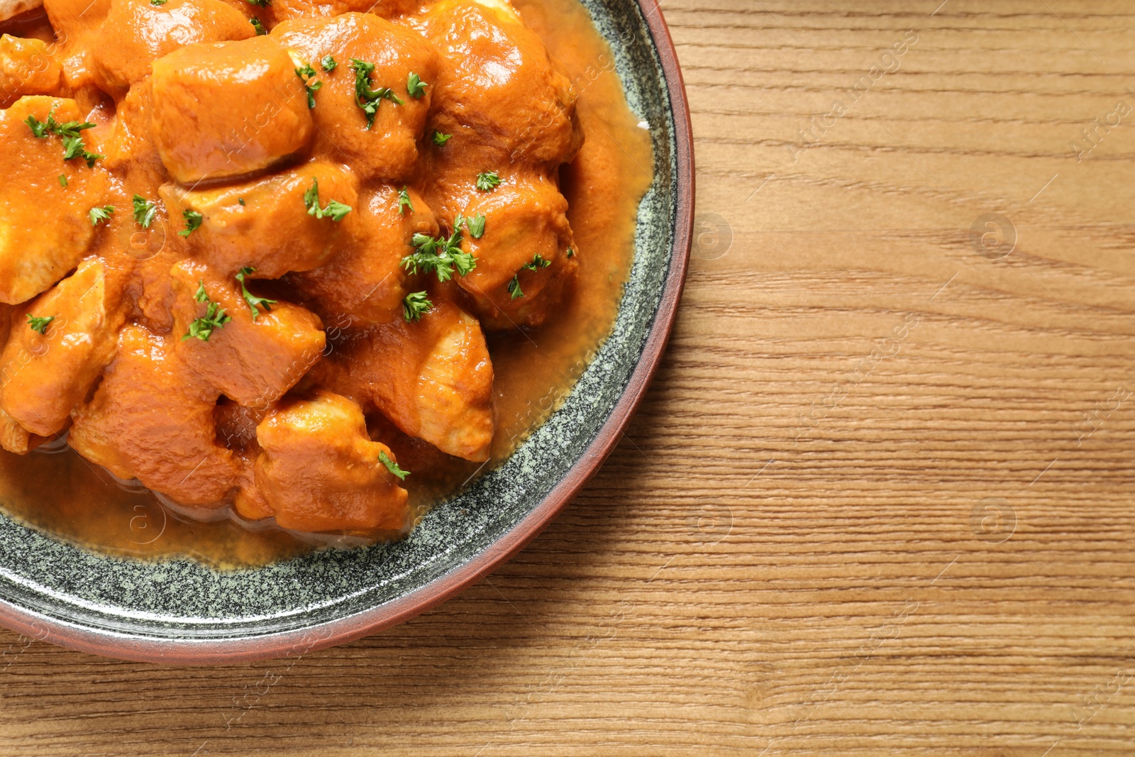 Photo of Delicious butter chicken on wooden table, top view with space for text. Traditional Murgh Makhani dish