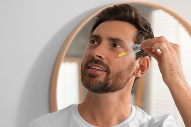 Photo of Handsome man applying cosmetic serum onto his face indoors. Space for text