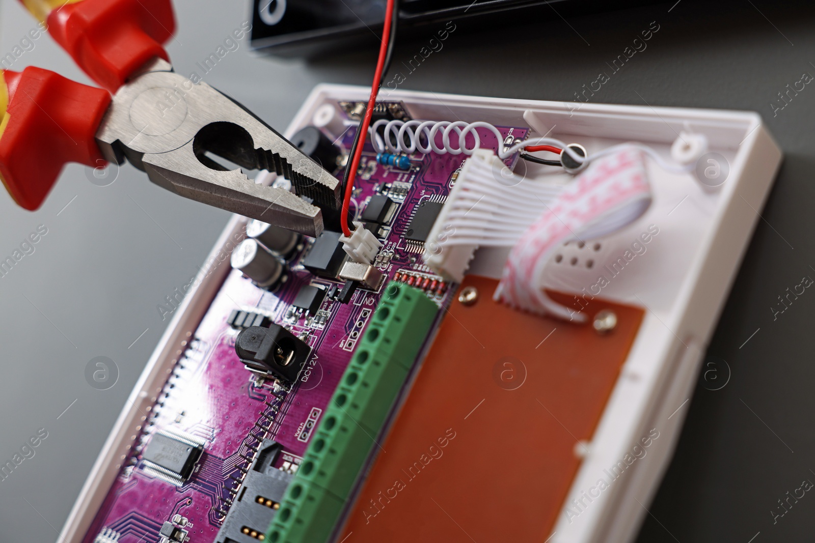 Photo of Using pliers while installing alarm system on gray wall, closeup