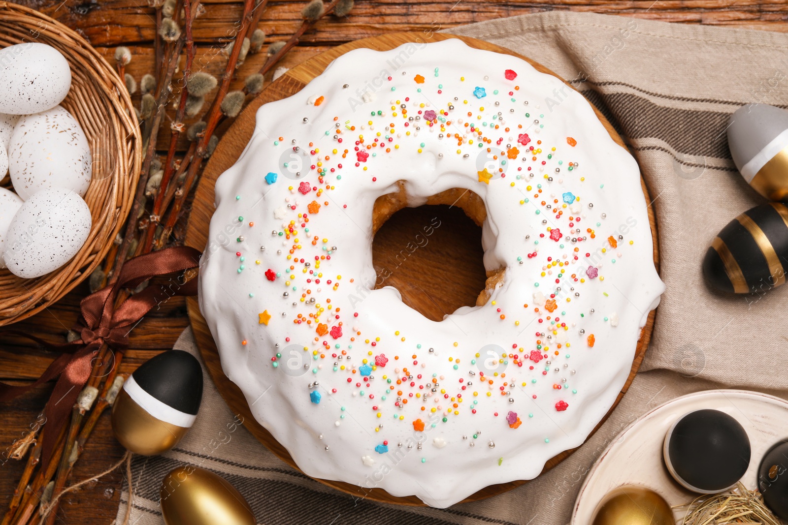 Photo of Delicious Easter cake decorated with sprinkles near painted eggs and willow branches on wooden table, flat lay