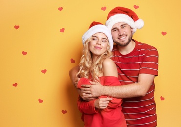 Photo of Young couple in Santa hats on color background. Christmas celebration