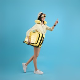 Photo of Happy female tourist with suitcase and travel pillow on light blue background
