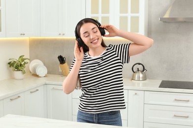 Happy woman in headphones enjoying music in kitchen