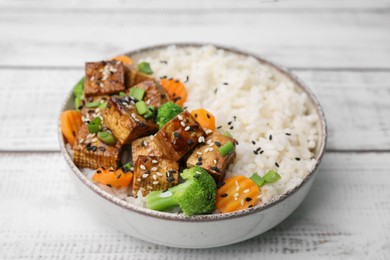 Photo of Bowl of rice with fried tofu, broccoli and carrots on white wooden table, closeup
