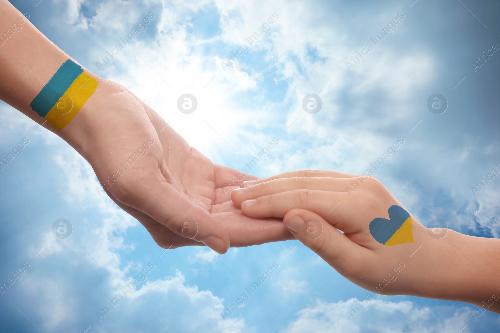 Image of Help for Ukraine. Woman and child holding hands with drawings of Ukrainian flag and beautiful blue sky on background, closeup