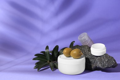 Cosmetic products and olives on lilac background, space for text
