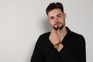 Handsome man in black shirt on light grey background, space for text