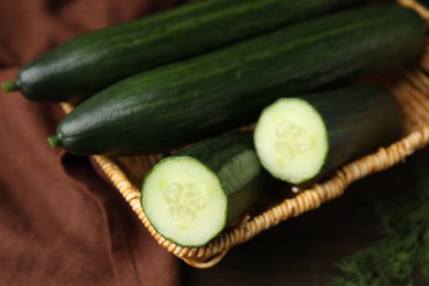 Photo of Fresh cucumbers in wicker basket on table, closeup