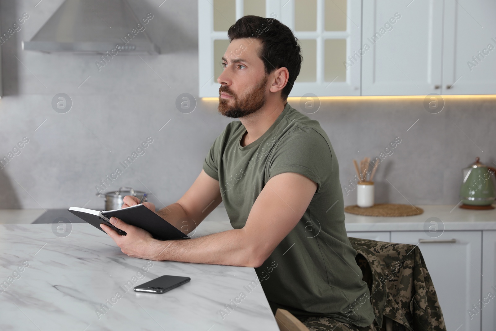 Photo of Soldier with notebook at white marble table in kitchen. Military service