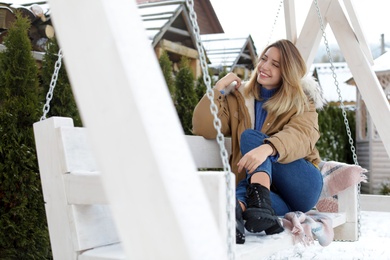 Photo of Young woman in warm clothes resting on outdoor swing. Winter vacation