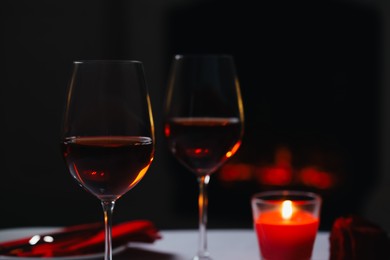 Glasses of red wine, rose flower and burning candle against blurred background, space for text. Romantic atmosphere