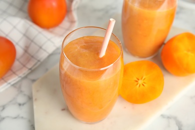 Photo of Tasty persimmon smoothie with straw on white table, closeup