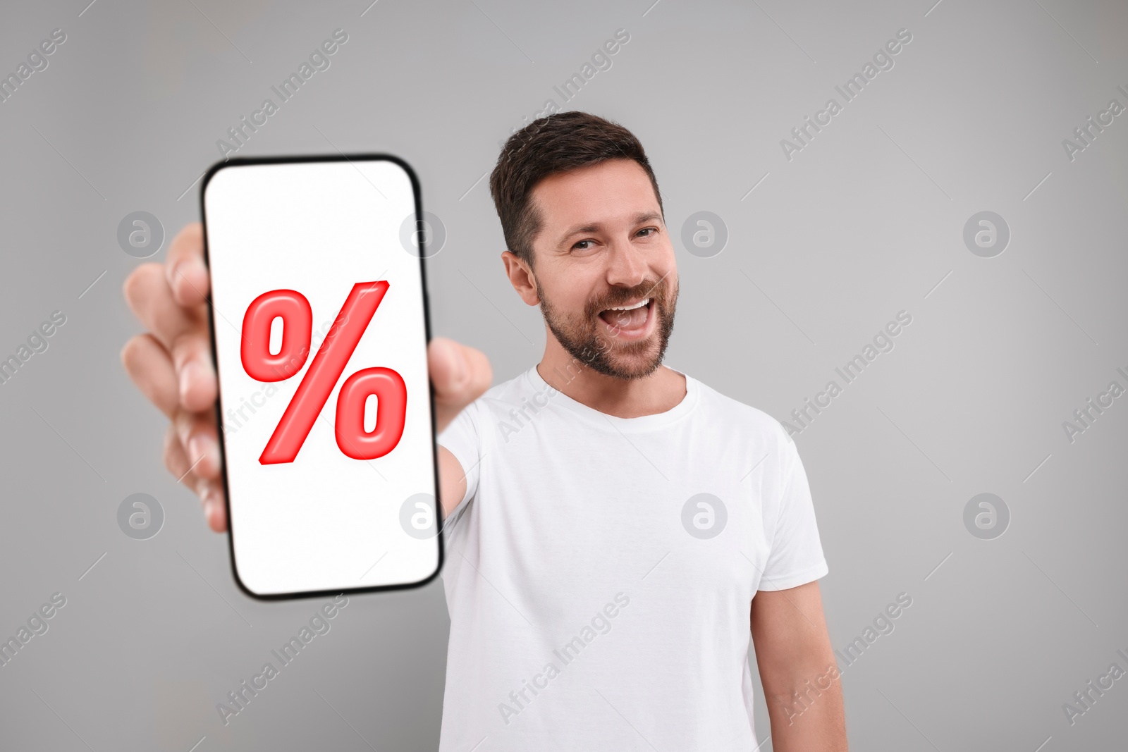 Image of Discount, offer, sale. Man showing mobile phone with percent sign on screen, grey background