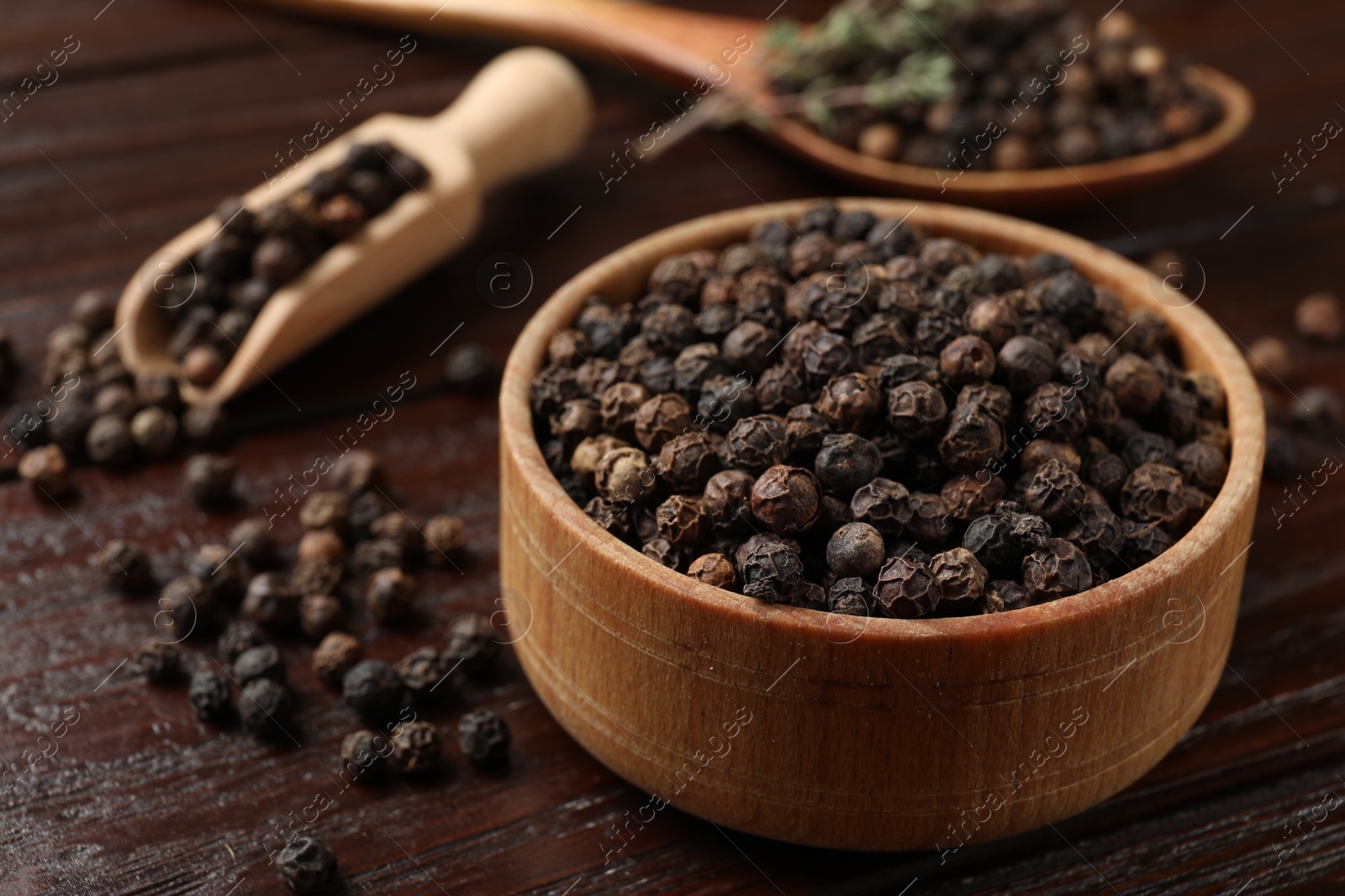 Photo of Aromatic spice. Black pepper in bowl and scoop on wooden table, closeup