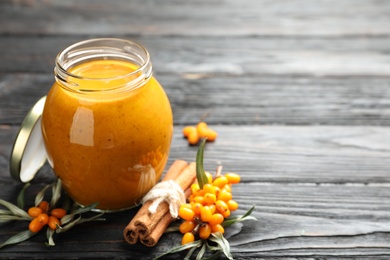 Delicious sea buckthorn jam and fresh berries on black wooden table. Space for text