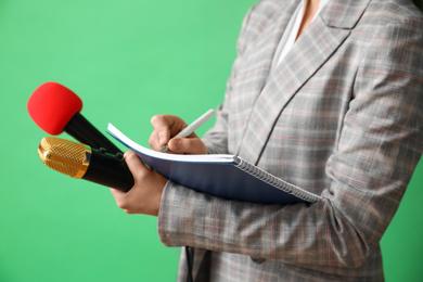 Journalist with microphones and notebook on green background, closeup