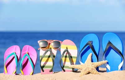 Composition with bright flip flops on sand near sea in summer. Beach accessories