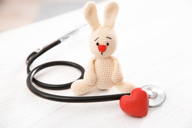 Photo of Toy bunny, stethoscope and heart on white wooden table. Children's doctor