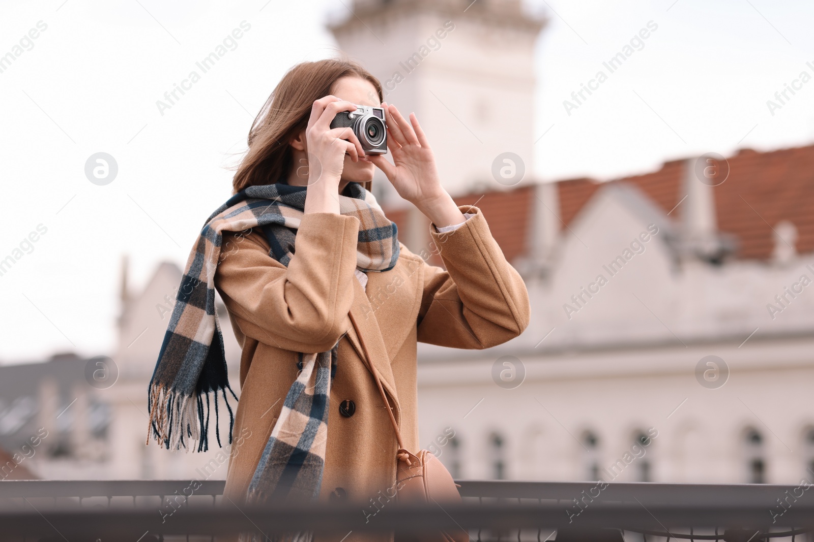 Photo of Beautiful woman in warm scarf taking picture with vintage camera outdoors