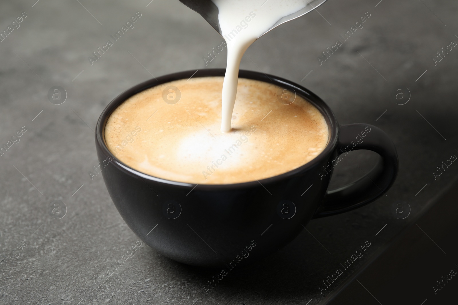 Photo of Pouring milk into cup of coffee on grey table, closeup