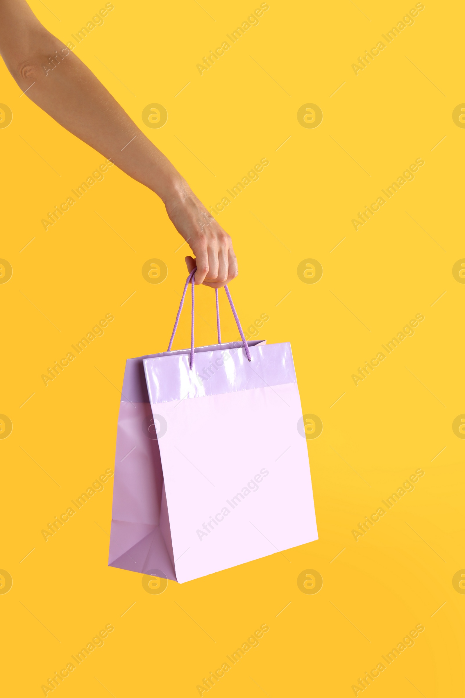 Photo of Woman with paper shopping bag on yellow background, closeup