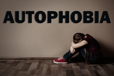 Upset little girl sitting alone near beige wall. Autophobia - fear of isolation
