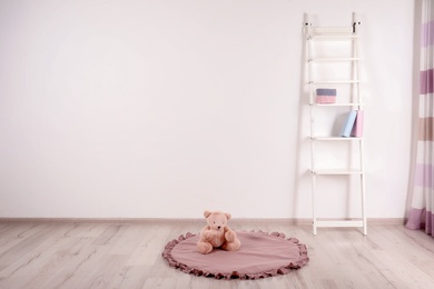 Photo of Teddy bear on floor and shelving unit near wall in child room. Space for text