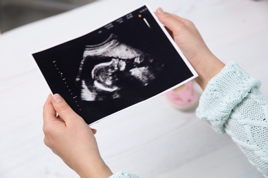Photo of Woman holding ultrasound photo of baby over table, closeup