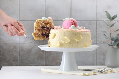 Woman taking slice of delicious cake at white wooden table, closeup