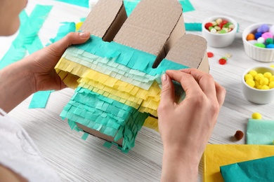 Photo of Woman decorating cardboard cactus at white wooden table, closeup. Pinata DIY